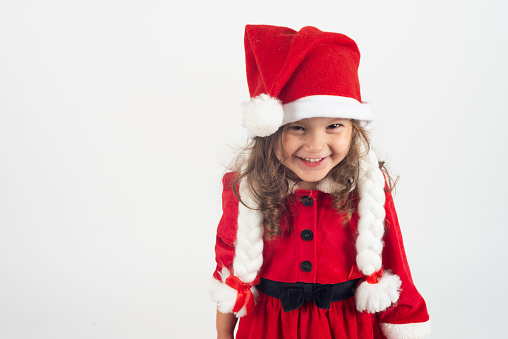 Little girl in Santa Claus costume is looking at camera with a toothy smile.