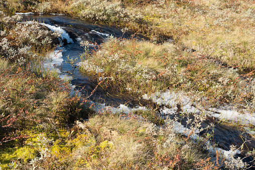 Hiking trail passes frozen lake and patches of snow in autumn colored high mountains after first snowfall of the season in Jotunheimen National Park in Norway. The snow of last season is still melting in some parts of the mountains. The image was captured with a full frame DSLR camera and a sharp fast lens.