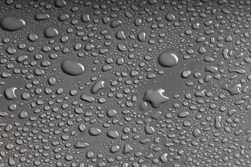 photo of irregularly shaped water droplets with various shapes on a black surface. lots of water drops on a plastic background