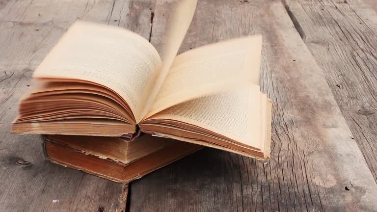 stack of old books on old grey wooden background. strong gusty wind turn the pages of an open book close up