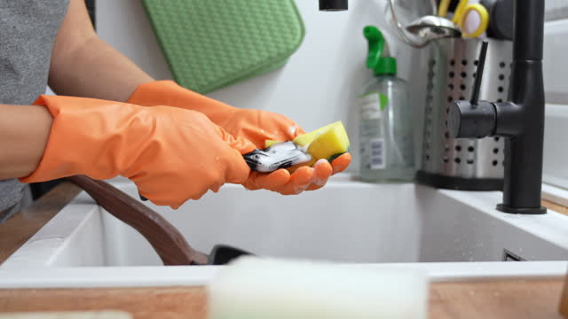 Unrecognizable woman cleaning the scraper with a cleaning sponge and liquid dishwasher detergent