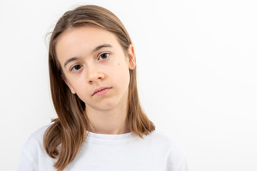 Tired teenage girl in a white T-shirt on a white background isolated, sad child, copy space.