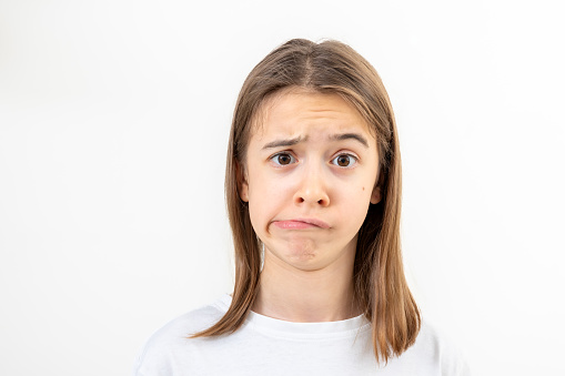 A teenage girl in a white T-shirt grimaces with displeasure on a white background isolated, doubts something, copy space.