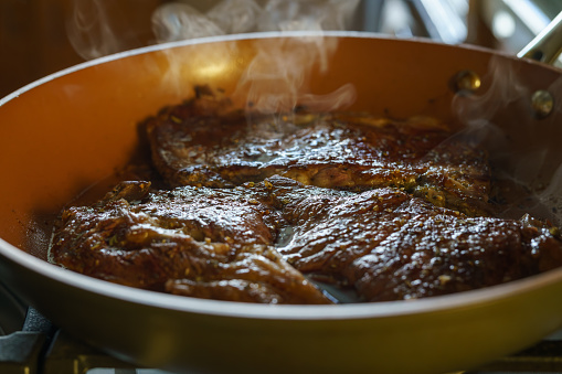 Beef steak sizzles on a hot frying pan, close-up moment of culinary perfection on the stove.