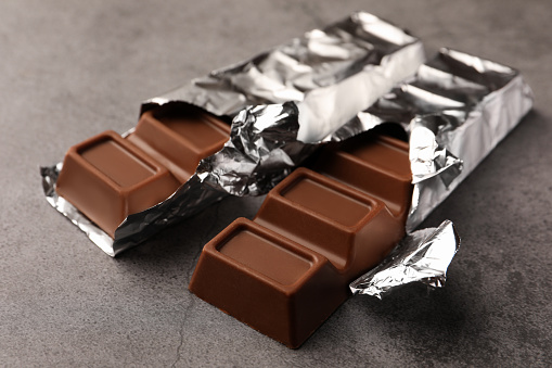 Tasty chocolate bars wrapped in foil on grey table, closeup
