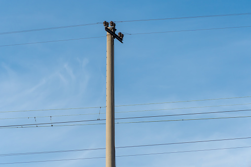 Electrified railway pole on blue sky background. Electric power supply lines on pillars along railway track. Technology of catenary wires. Details structure of voltage system. Equipment of railroad.