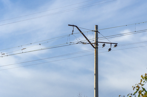 Electrified railway pole on blue sky background. Electric power supply lines on pillars along railway track. Technology of catenary wires. Details structure of voltage system. Equipment of railroad.