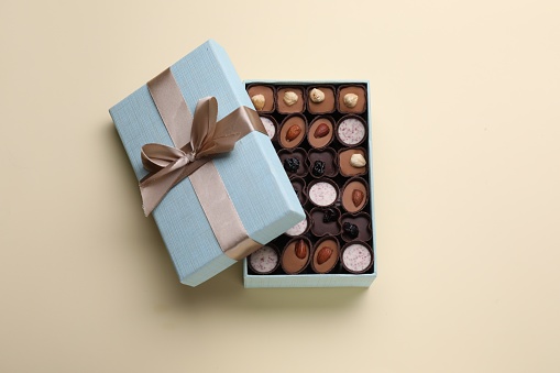 Open box of delicious chocolate candies on beige background, top view