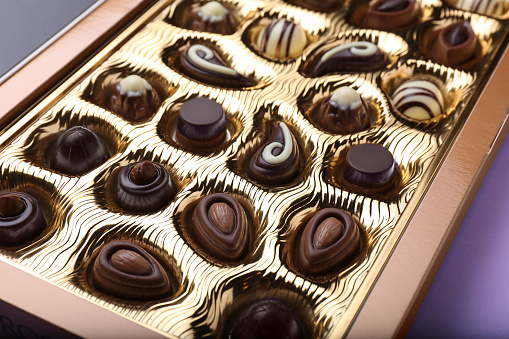 Box of delicious chocolate candies on violet background, closeup