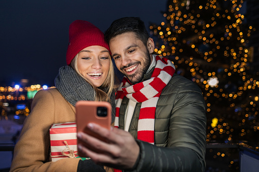 Young couple looking at the phone outdoors, during Christmas