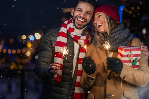 Young couple holding sparkles while celebrating Christmas outdoors