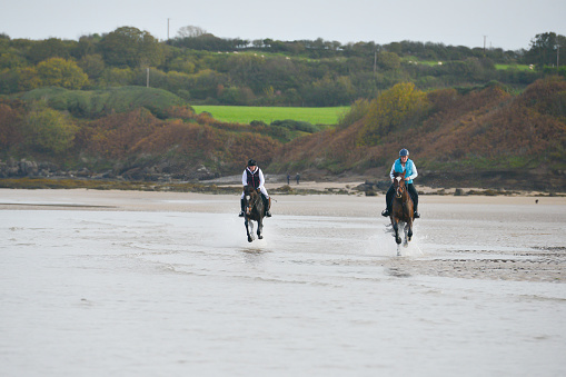 Mother and daughter enjoy a race on their horses  across an empty beach in Wales UK enjoying the freedom to move at speed and share the joy of riding .