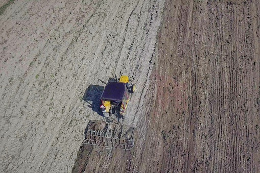 A farmer on a tractor with a seeder sows grain in plowed land in a private field in the village area. Mechanization of spring field work. Farmer's everyday life. Processing of land. The agrarian.