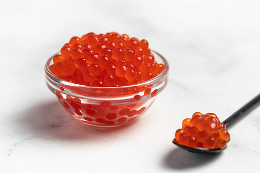 Red fish caviar on a spoon in glass bowl. Raw seafood. Luxury delicacy food. Flat lay, top view, copy space.