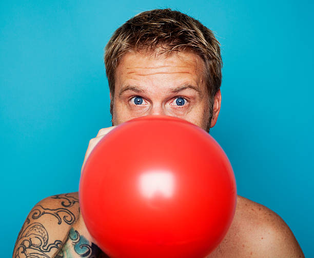 Blonde man blowing up a red balloon stock photo