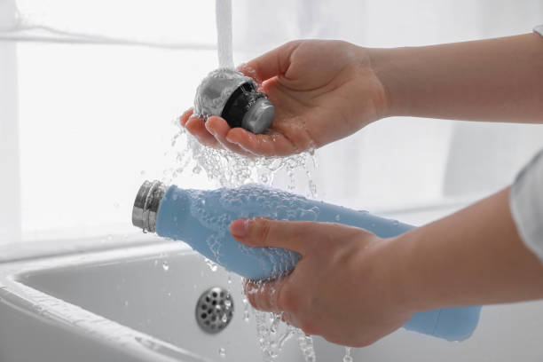 Woman washing thermo bottle in kitchen, closeup