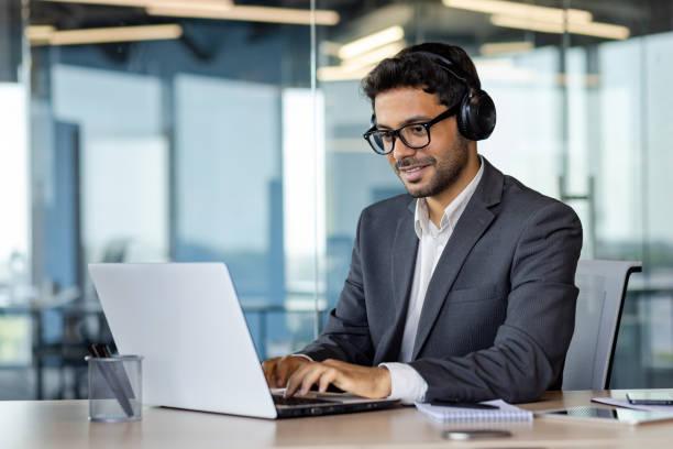 istock Successful indian programmer working inside office with laptop, man in headphones and business suit, typing code on keyboard, developing new software 1806223785