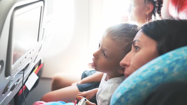 Baby boy sitting on seat on airplane and using remote controller with screen for on board entertainment. Multimedia system with game, film, music. Control joystick in hands child. Leisure activity.