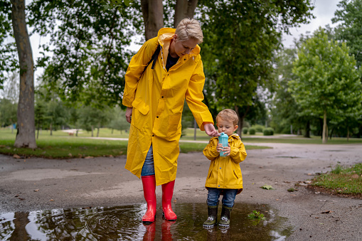 Beautiful young mother with little son walking in the street after a rain. Vertical view