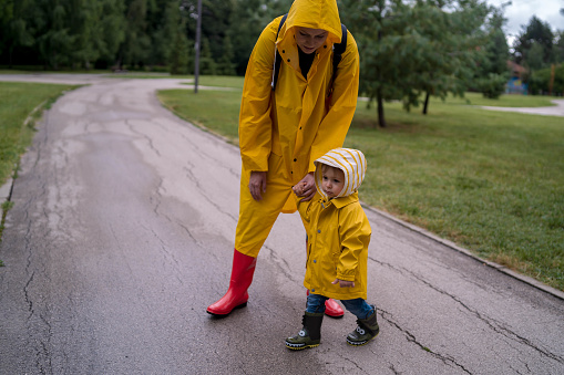 Beautiful young mother with little son walking in the street after a rain. Vertical view