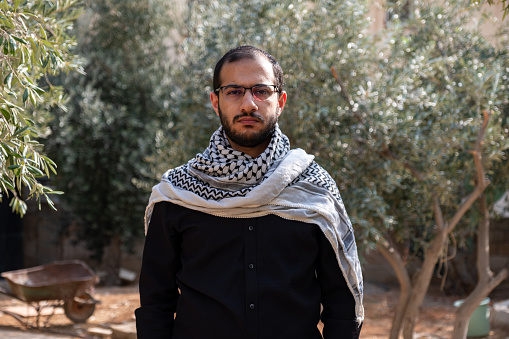 Retrato para hombre que usa keffiyeh en campo de olivos con fondo negro y camisas negras también con expresión facial enojada photo