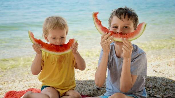 istock Two little boy having fun and playing while eating watermelons on sunny sandy sea beach 1806269125