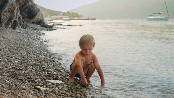 garotinho bonito se divertindo na praia do mar e jogando pedras nas ondas do mar - throwing stone little boys child - fotografias e filmes do acervo