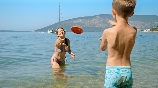 Happy mother with son playing frisbee on the sea beach. Family holiday, vacation and fun summertime of children and parents