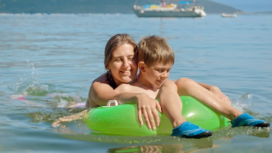 Portrait of cheerful boy and mother enjoying swimming in the sea with inflatable ring. Family holiday, vacation and fun summertime of children and parents