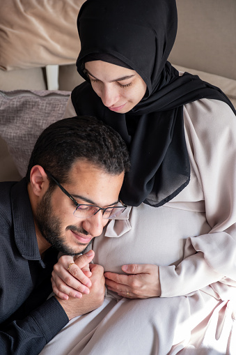 Arabian man is listening to his beautiful pregnant wife's tummy and smiling