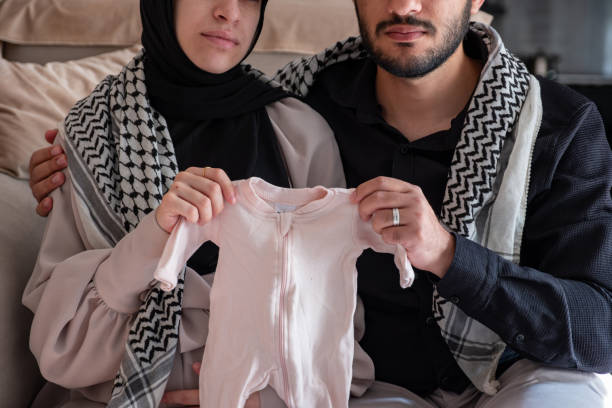 Husband and his wife holding newborn clothes for there dead child  while wearing palestinian keffiyeh in living room Husband and his wife holding newborn clothes for there dead child  while wearing palestinian keffiyeh in living room kaffiyeh stock pictures, royalty-free photos & images