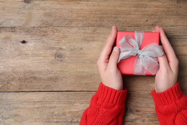 istock Christmas present. Woman holding gift box at wooden table, top view. Space for text 1806282474