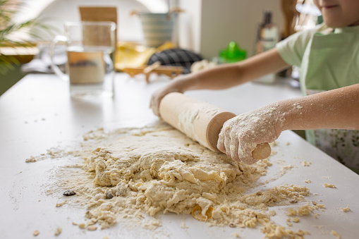 Little boy rolling dough with rolling pin in kitchen at home