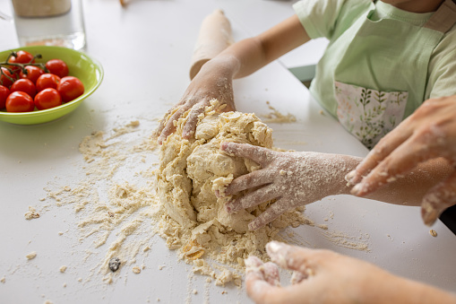 Little boy and his grandmother kneading dough together in kitchen at home