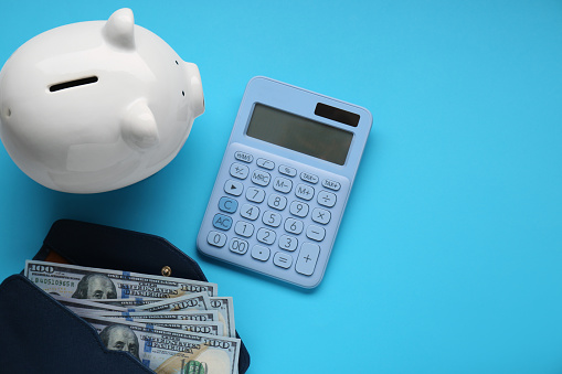 Piggy bank, calculator and wallet with banknotes on light blue background, flat lay. Space for text