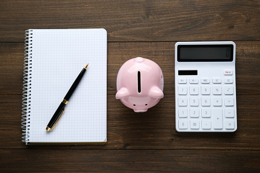 Calculator, piggy bank and notebook on wooden table, flat lay