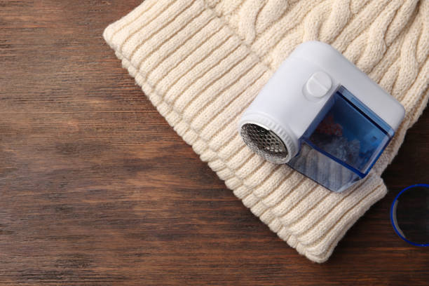 istock Modern fabric shaver and white knitted hat on wooden table, top view. Space for text 1806317068