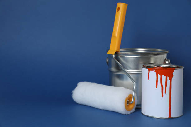 istock Cans of orange paint and brush roller on blue background. Space for text 1806325777