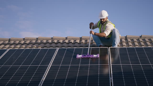 Technician cleaning solar panel on roof, maintenance and renewable energy or electricity. Engineer, man mop photovoltaic cell and dust, dirt and improve performance,  power production and service