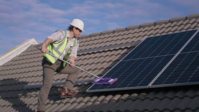 Engineer cleaning solar panel on roof, maintenance and renewable energy or electricity. Technician, man mop photovoltaic cell and dust, dirt and improve performance,  power production and service