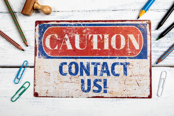 istock Contact Us. Metal CAOTION plate with text on a white wooden background 1806343903