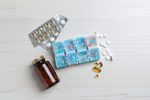 Weekly pill box and bottle with medicaments on white wooden table, flat lay