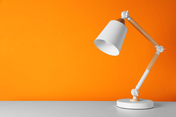 istock Stylish modern desk lamp on white table near orange wall, space for text 1806373128