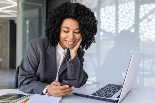 istock Successful businesswoman at workplace inside office using phone, female worker reading message and smiling, african american woman holding smartphone using online application 1806378529