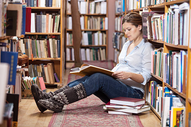 Young pregnant woman reading book in library stock photo