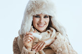 smiling stylish woman in winter coat and fur hat on white