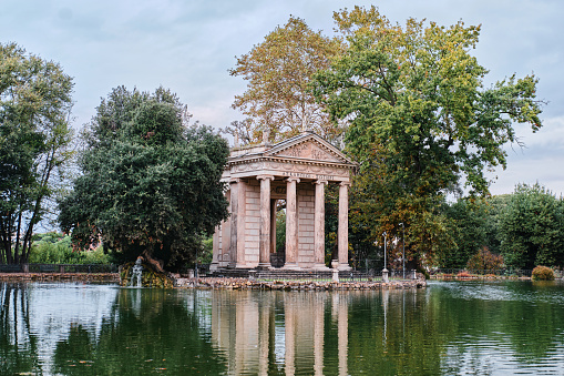 The temple of Antoninus and Faustina in the park of Villa Borghese, in the green heart of Rome near the Pincio Gardens. This temple, made up of fragments of temples from the ancient Roman Forums, was built in 1792 for the Borghese family by the architect Cristoforo Unterperger. Considered the green lung of Rome, Villa Borghese is the largest public park in the city with almost 80 hectares of extension, where residents and tourists can spend hours of relaxation and silence among tree-lined avenues, ponds and Italian and English-style gardens surrounded by trees and ancient pines. The area of the Villa Borghese includes the extension of ancient gardens the of the Borghese family since 1580, while the current arrangement of the park was completed in 1903 in neoclassical style. In 1980 the historic center of Rome was declared a World Heritage Site by Unesco. Super wide angle image in high definition format.