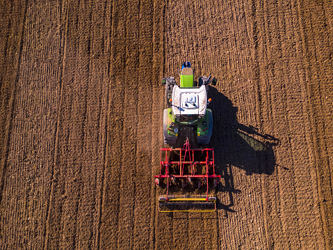 Aerial view of a green tractor plowing a field leaving tracks on the field