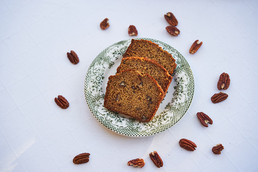 Top view on three slices of homemade banana bread with pecan nuts on the small porcelain plate isolated on the table with white table colth. Healthy, lowcarb and balanced dish ideal for breakfast.