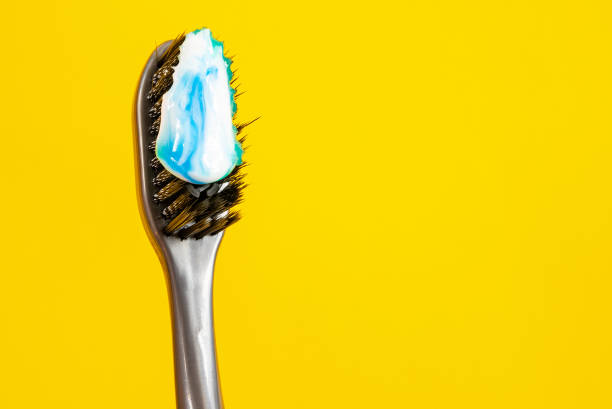 istock Black bristled toothbrush with white and blue toothpaste on yellow background 1806432994